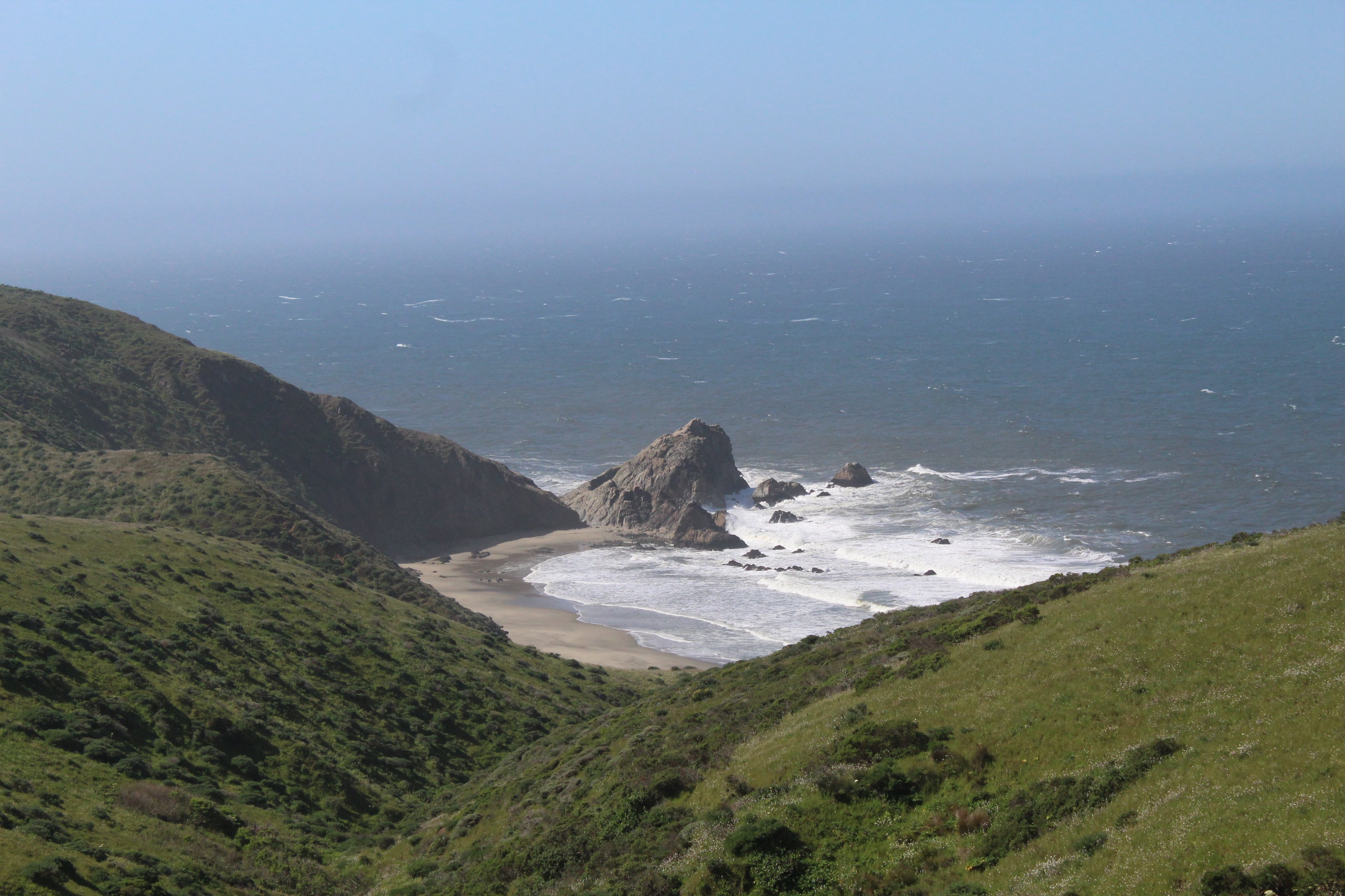 A giant rock at the tip of a bay at the base of large bright green fields available on canvas print